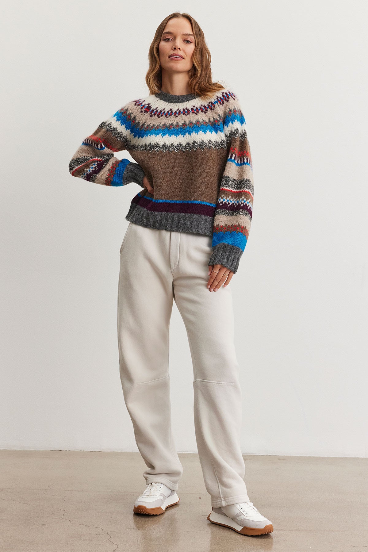   A person wearing a vibrant KELLA ALPACA FAIR ISLE SWEATER by Velvet by Graham & Spencer and cream pants stands on a plain background. 