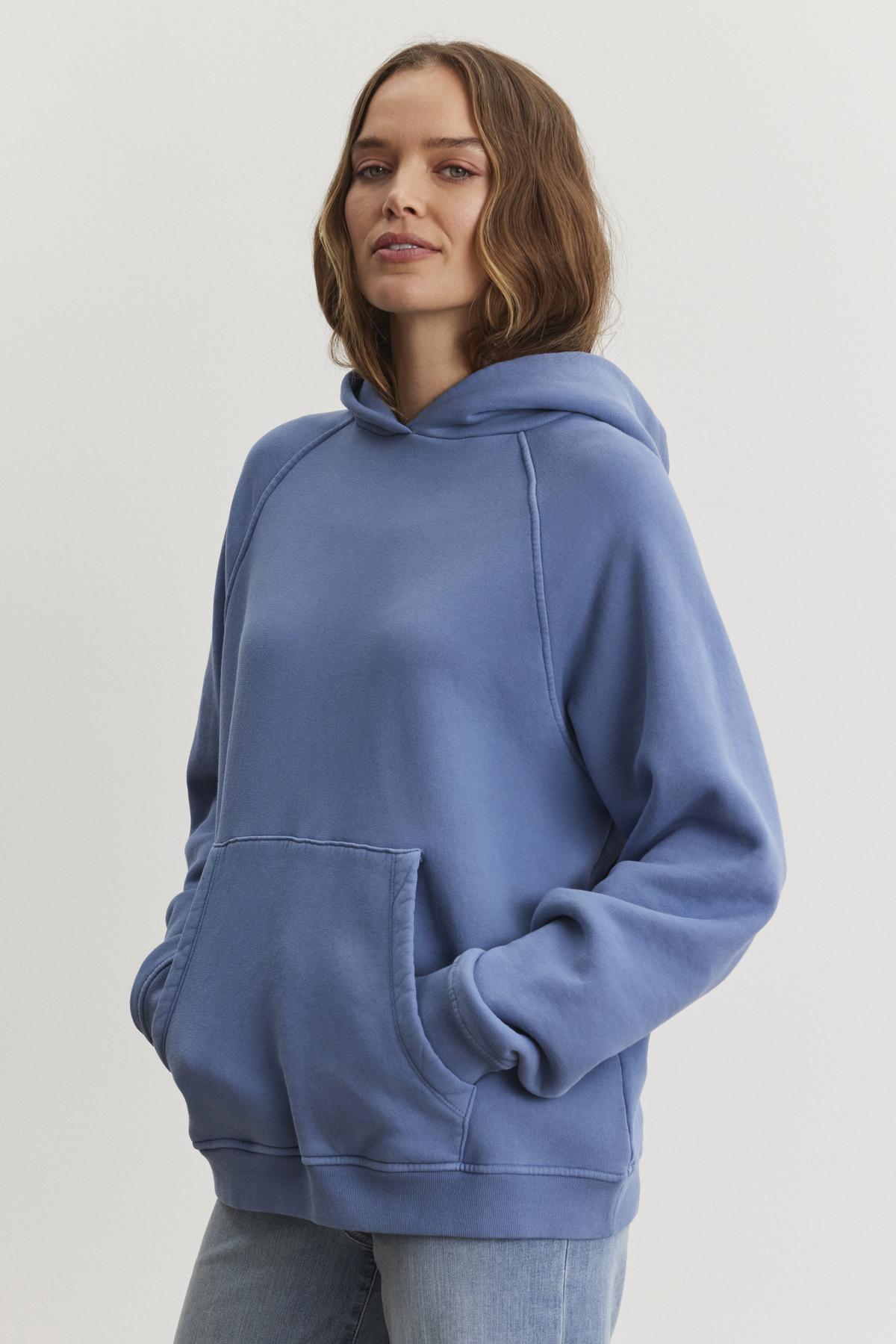 A person wearing the oversized VERONICA HOODIE by Velvet by Graham & Spencer, crafted from cotton fleece with hands snugly tucked in its front pocket, stands against a plain background.-38512021700801
