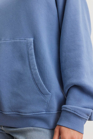 Close-up of a person wearing the VERONICA HOODIE by Velvet by Graham & Spencer, featuring a blue cotton fleece pullover style with a front pocket, paired with light blue jeans.