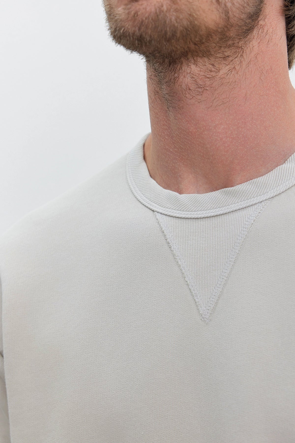   Close-up of a person wearing the ISAMU SWEATSHIRT by Velvet by Graham & Spencer, made from heavyweight cotton fleece in light grey, showcasing the neckline and part of their face and neck. 