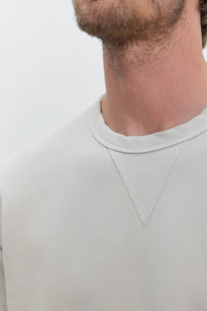 Close-up of a person wearing the ISAMU SWEATSHIRT by Velvet by Graham & Spencer, made from heavyweight cotton fleece in light grey, showcasing the neckline and part of their face and neck.