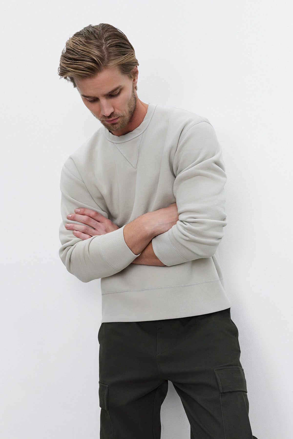   A man with short hair, dressed in an ISAMU SWEATSHIRT by Velvet by Graham & Spencer and dark pants, stands against a plain white background with his arms crossed. 