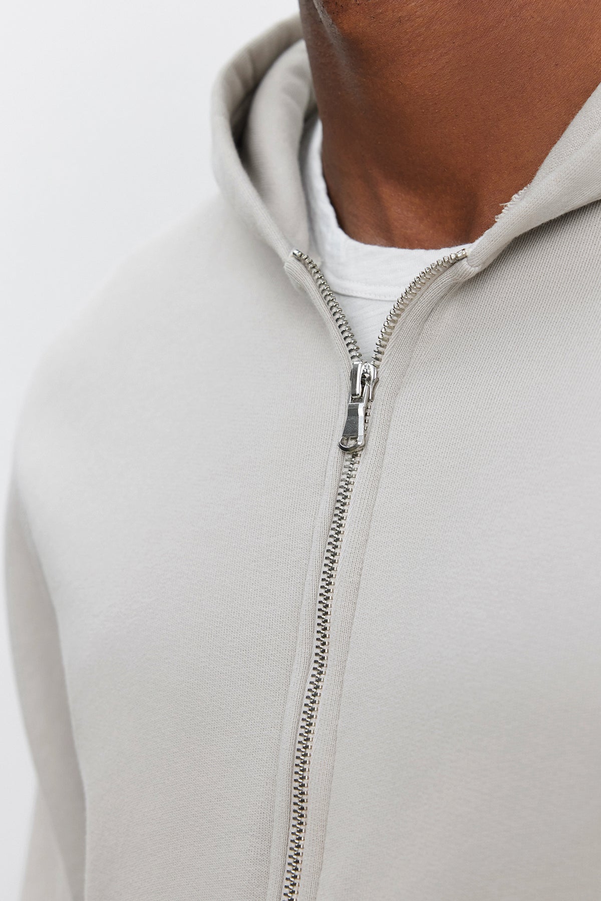 Close-up of a person wearing the REN HOODIE from Velvet by Graham & Spencer, a light gray, cotton fleece, full-zip hoodie over a white t-shirt, focusing on the zipper and chest area.-37893921046721