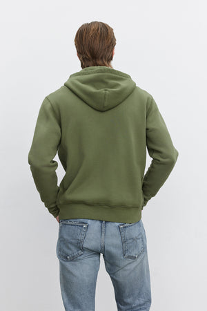 A person is seen from behind, wearing the REN HOODIE by Velvet by Graham & Spencer and faded blue jeans for a vintage look.