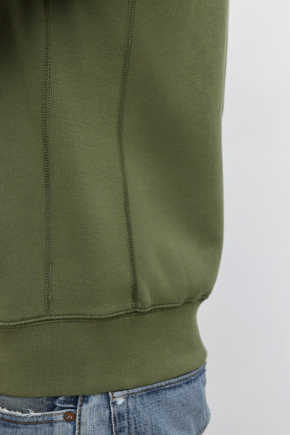   Close-up of a person wearing the REN HOODIE by Velvet by Graham & Spencer and faded blue jeans. The cotton fleece sweatshirt covers most of the person's torso, giving off a vintage look. 