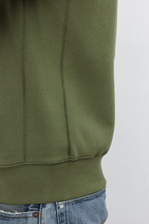 Close-up of a person wearing the REN HOODIE by Velvet by Graham & Spencer and faded blue jeans. The cotton fleece sweatshirt covers most of the person's torso, giving off a vintage look.