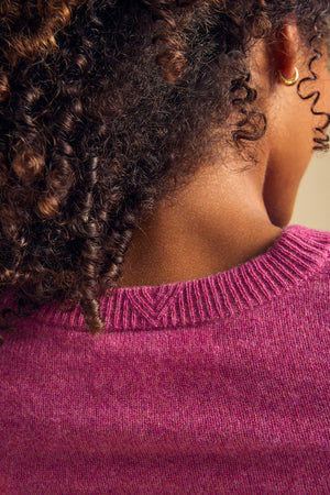 Close-up of the back of a person with curly hair wearing the textured pink AYLINA CASHMERE CARDIGAN by Velvet by Graham & Spencer and a small gold hoop earring.