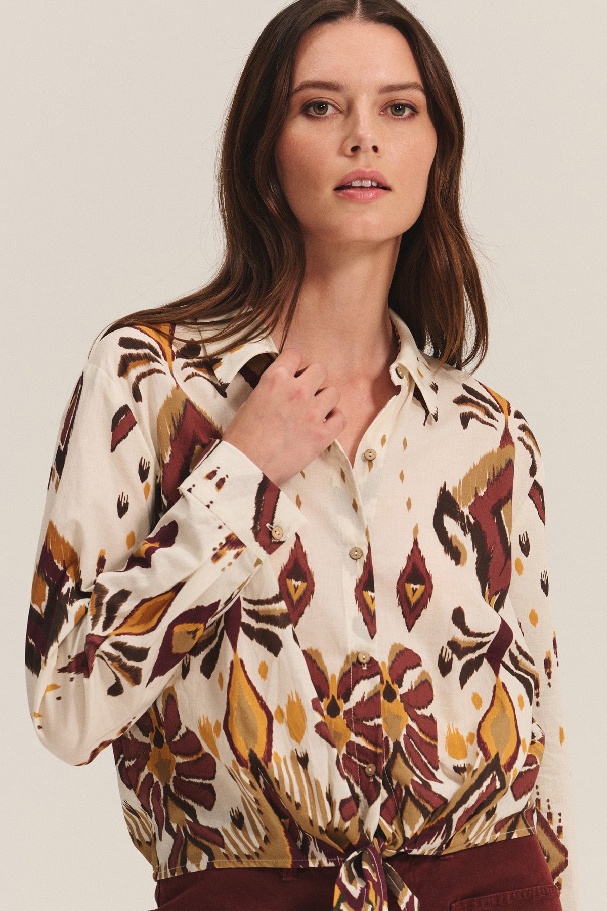 A woman wears the KAYLA TOP by Velvet by Graham & Spencer, a patterned cotton-viscose blend button-down featuring maroon, yellow, and brown designs, standing against a neutral background.