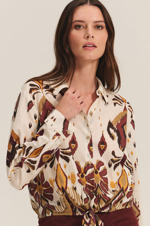 A woman wears the KAYLA TOP by Velvet by Graham & Spencer, a patterned cotton-viscose blend button-down featuring maroon, yellow, and brown designs, standing against a neutral background.