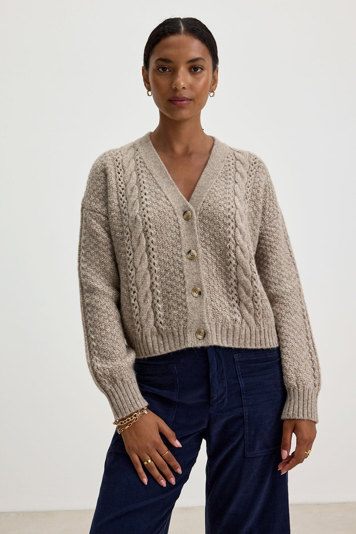   A person wearing the IZZY CARDIGAN by Velvet by Graham & Spencer and dark blue pants stands in front of a plain background. 