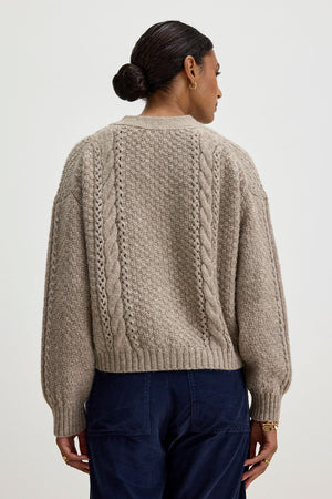 A person with dark hair in a bun is wearing the IZZY CARDIGAN by Velvet by Graham & Spencer along with dark blue pants, seen from the back.