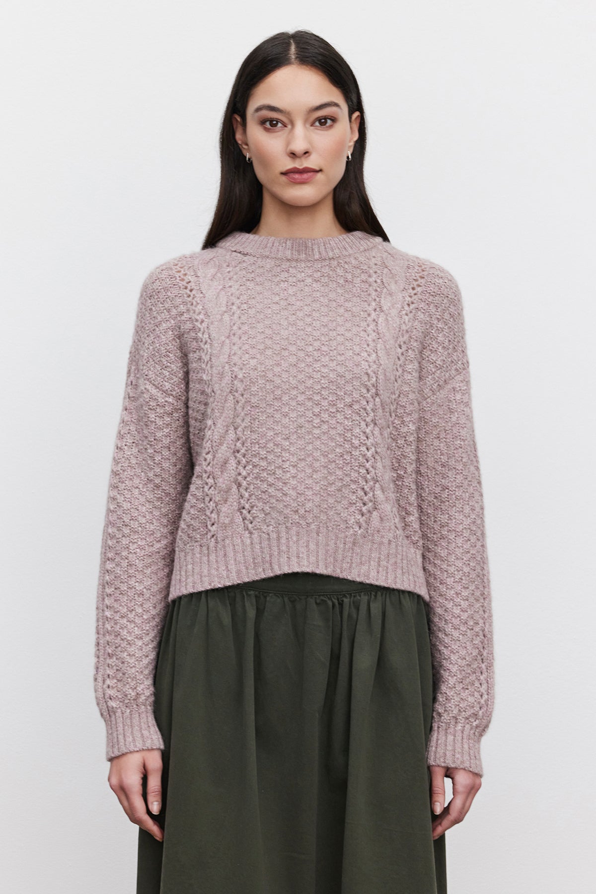 A woman with long dark hair wears a MARLEY SWEATER, a light purple alpaca blend by Velvet by Graham & Spencer, paired with an olive green skirt, standing against a plain white background.-37856196788417