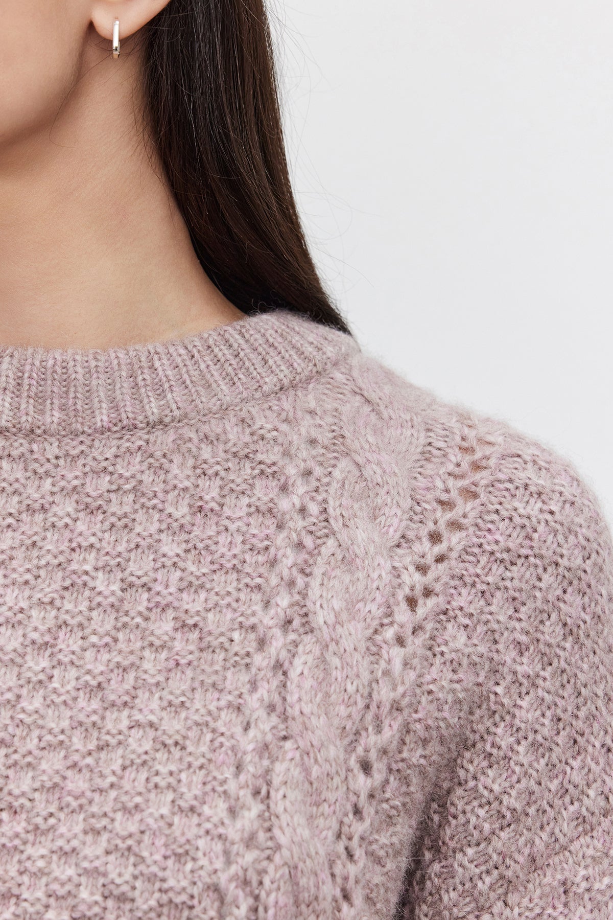 Close-up of a person wearing the MARLEY SWEATER by Velvet by Graham & Spencer, showcasing its light purple alpaca blend fabric with a braided pattern and accessorized with small hoop earrings, capturing only the shoulder and part of the face.-37856196821185