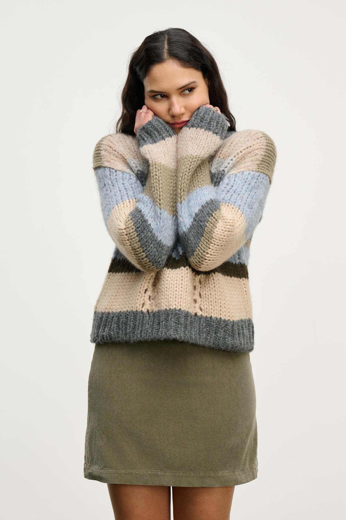 A woman wearing the RINA ALPACA SWEATER by Velvet by Graham & Spencer—featuring a boxy fit and blue, gray, and beige stripes—pairs it with an olive green skirt, standing against a plain light background.-39815256572097