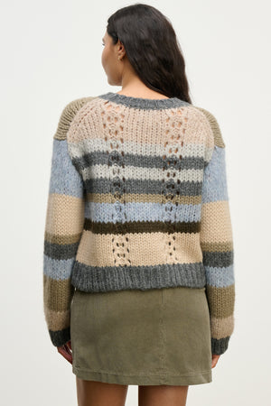A woman is seen from behind wearing the RINA ALPACA SWEATER by Velvet by Graham & Spencer, a boxy fit, striped piece in neutral tones, paired with an olive green skirt.