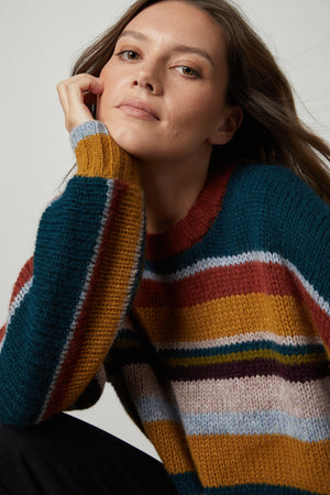 A woman is posing for a photo wearing the Velvet by Graham & Spencer SAMARA STRIPED CREW NECK SWEATER, showcasing the cozy elegance of her outfit.