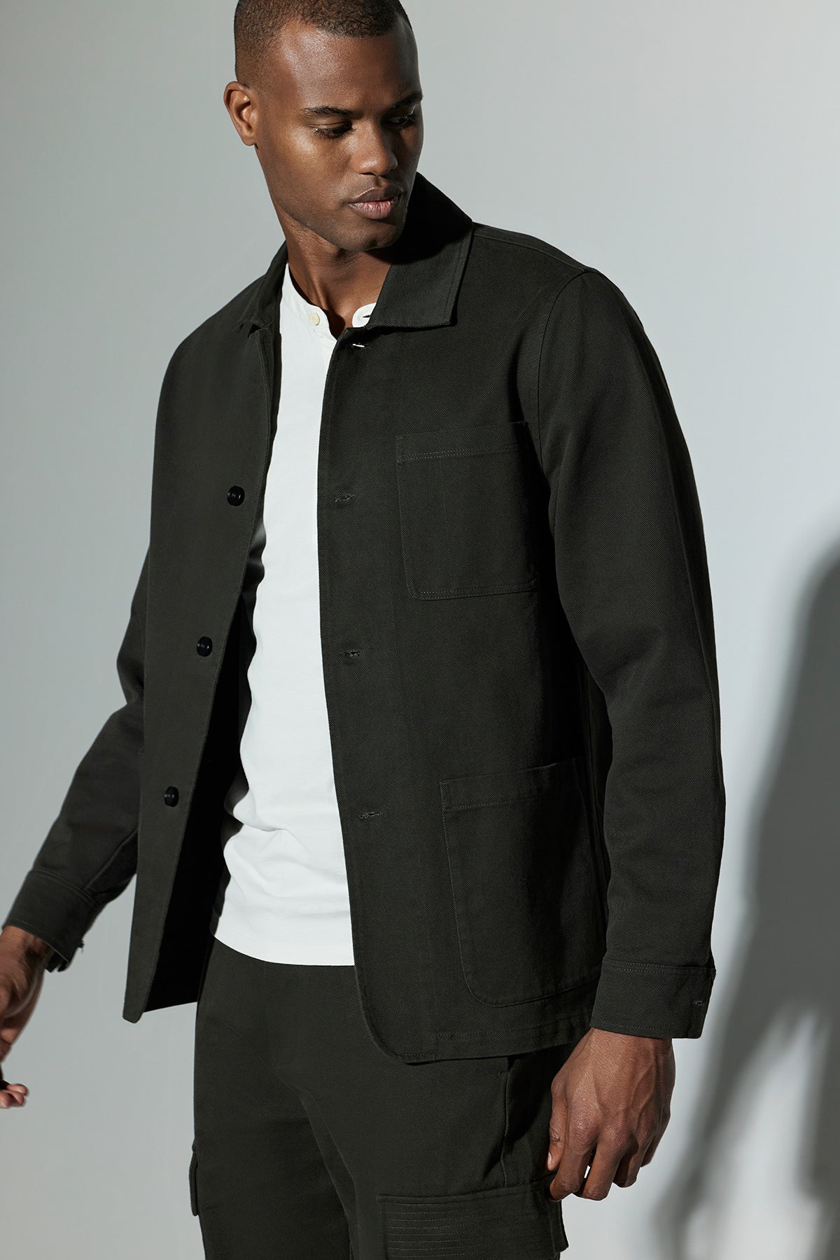   A man wearing the Velvet by Graham & Spencer BARCLAY CHORE JACKET, a mid-weight cotton lyocell twill jacket in dark green, over a white shirt poses against a neutral background. 