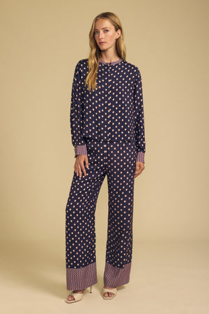 A woman wears a long-sleeved button-down shirt and matching navy blue diamond print CAROL PRINTED PANT by Velvet by Graham & Spencer, both featuring patterned cuffs and hems.