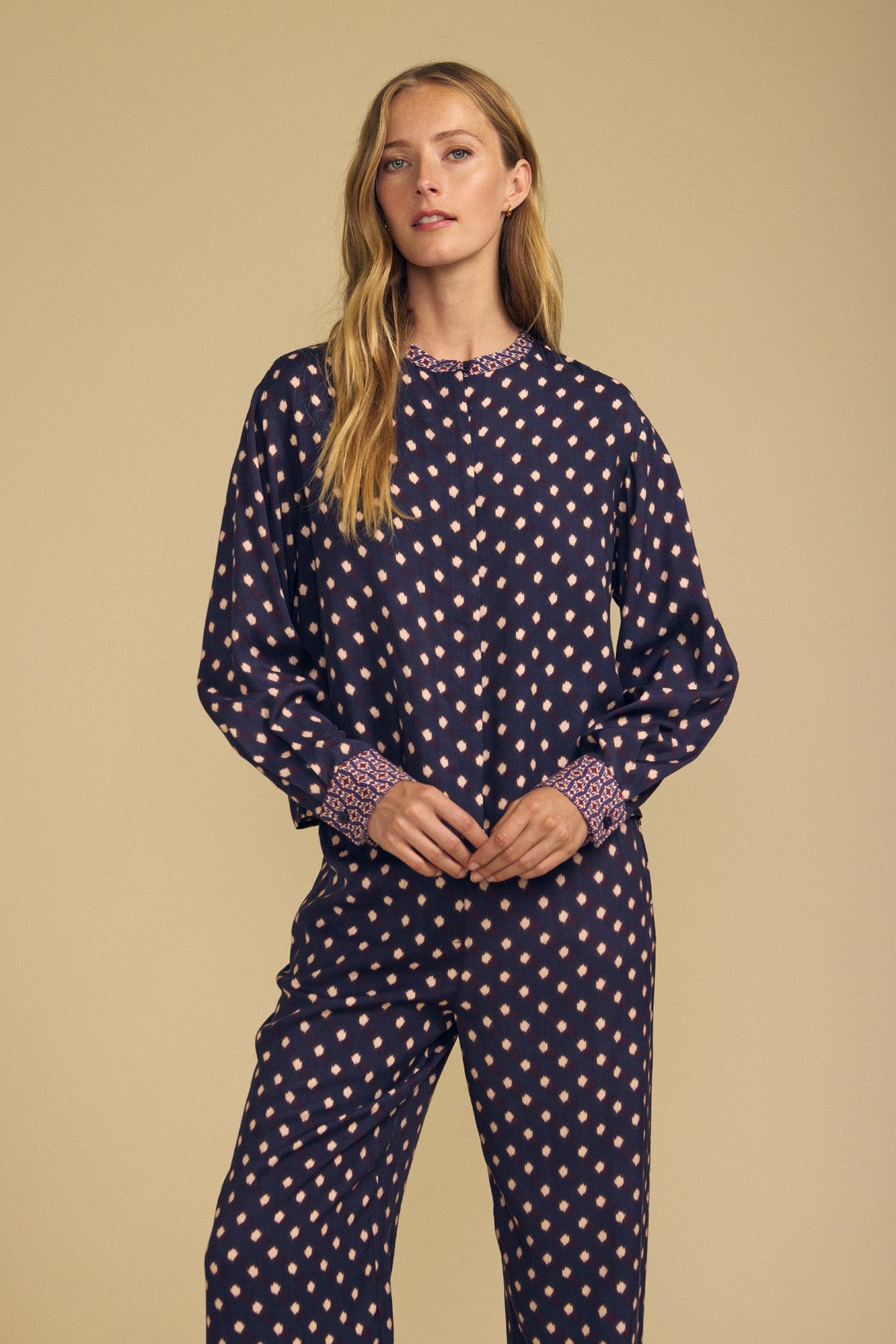 A woman wearing a dark blue ERIKA PRINTED BLOUSE and matching pants with a small pink diamond pattern and a patterned border print at the collar and cuffs.-46488190124225