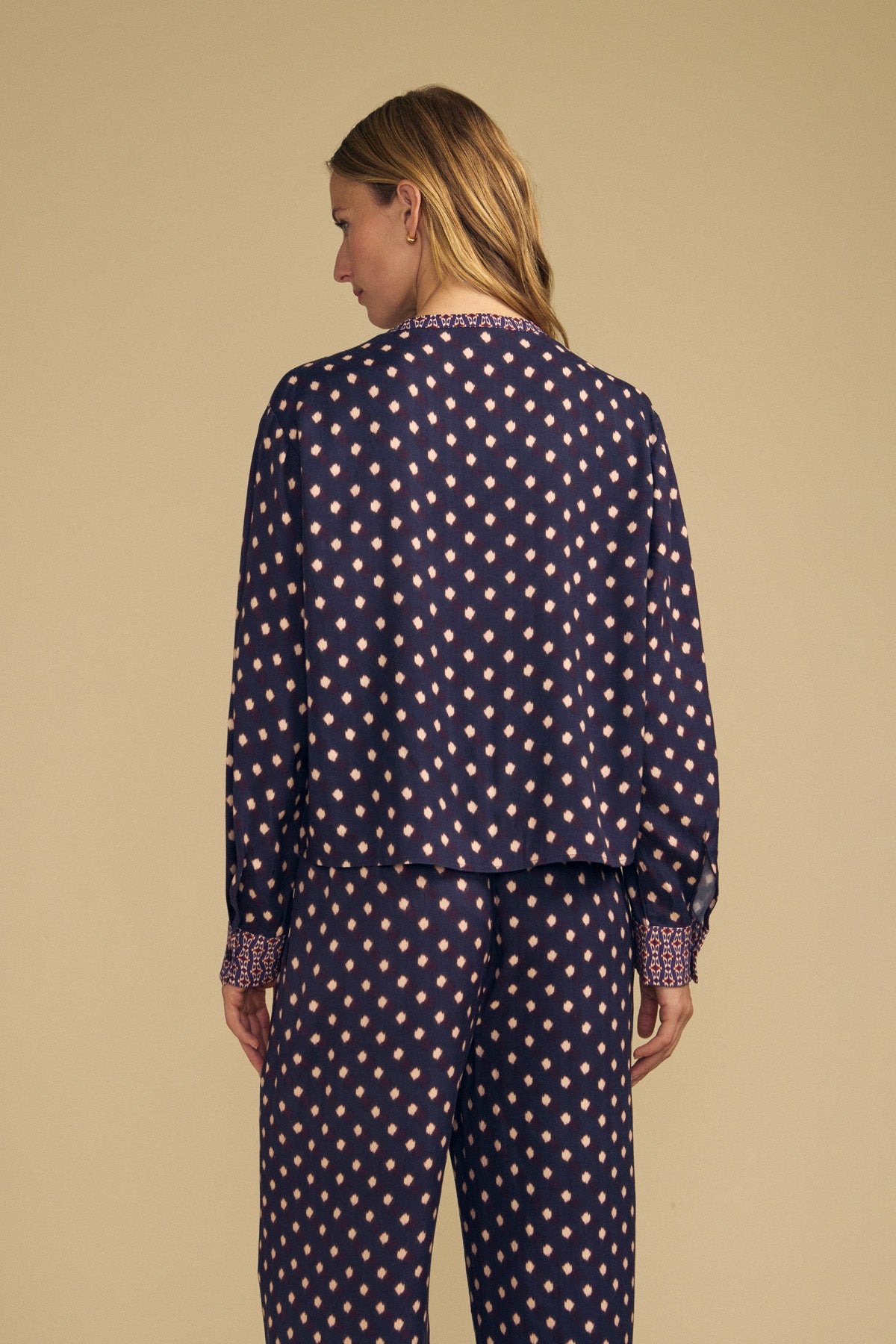 A woman wears a dark navy blue ERIKA PRINTED BLOUSE and matching pants, both featuring a repeating light pink diamond pattern.-46488189927617