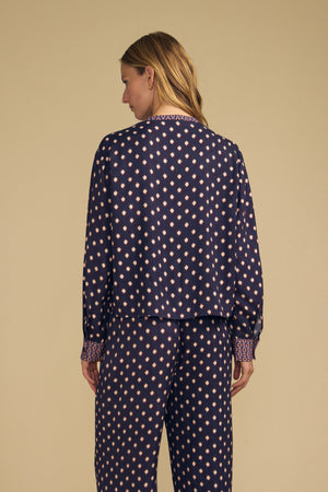A woman wears a dark navy blue ERIKA PRINTED BLOUSE and matching pants, both featuring a repeating light pink diamond pattern.