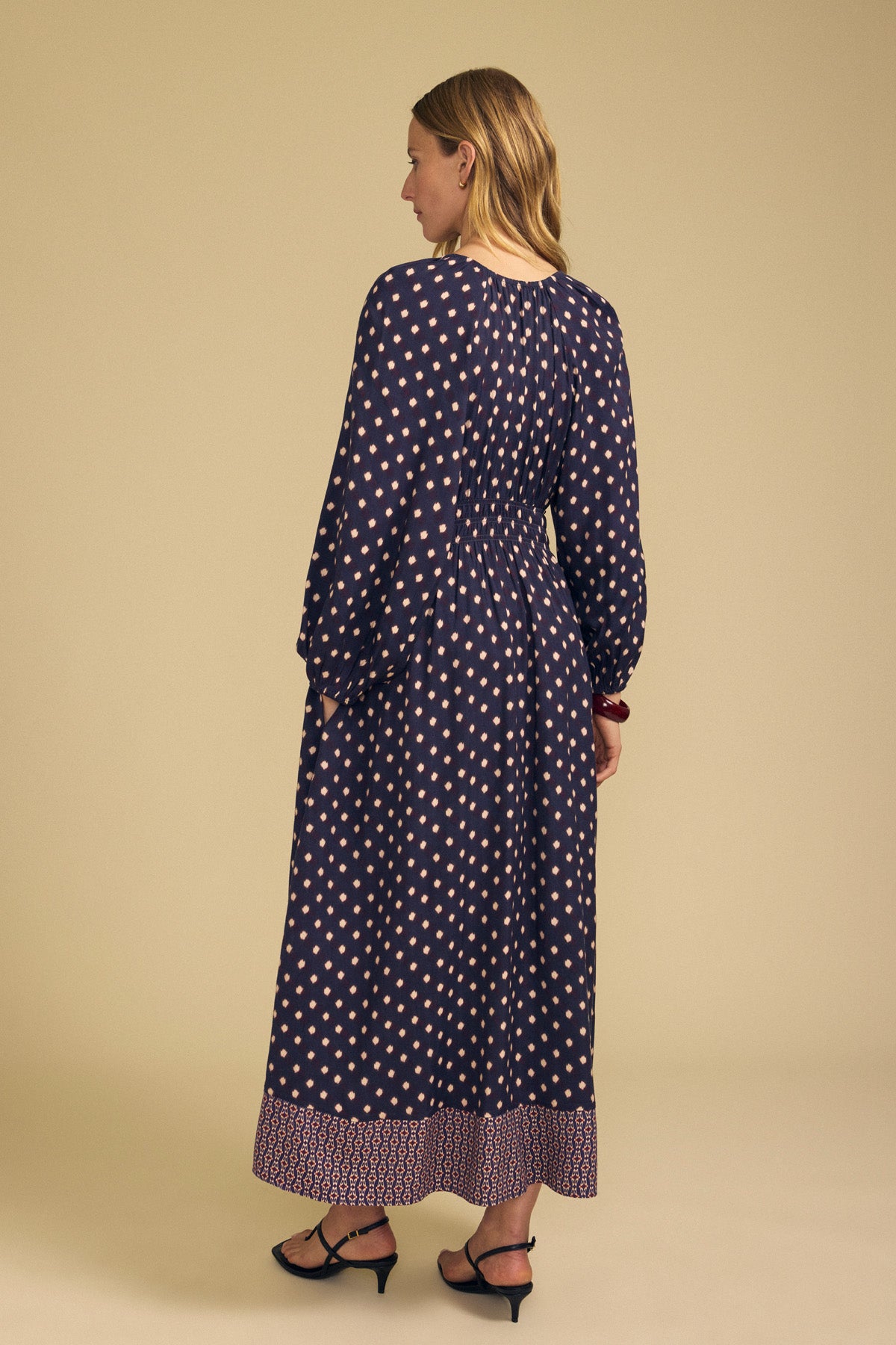 A woman from behind wearing a navy blue long-sleeved MALLORY PRINTED DRESS by Velvet by Graham & Spencer, featuring a light-colored diamond print and a patterned border hem.-46489566216385