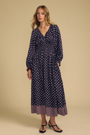 Woman wearing a navy blue MALLORY PRINTED DRESS featuring a repeating diamond print and a decorative border print hem.