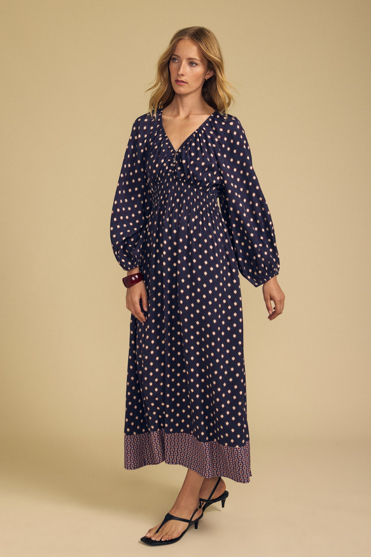 The Velvet by Graham & Spencer MALLORY PRINTED DRESS is a long-sleeved, navy blue midi dress featuring a repeating diamond print, a smocked bodice, and a distinct border print at the hem.-46489565921473