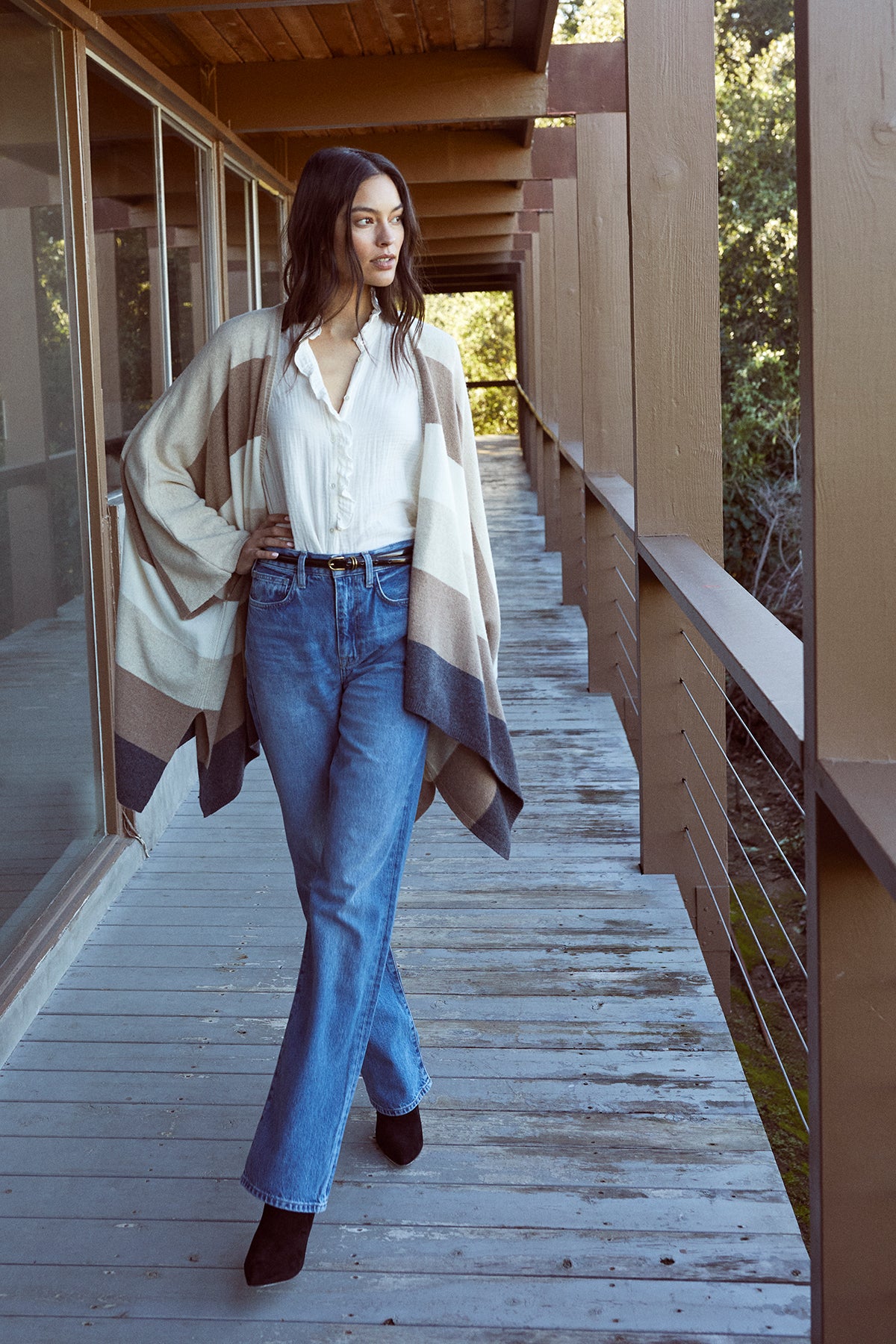 A woman wearing jeans and a cardigan TRISHA COTTON GAUZE TOP by Velvet by Graham & Spencer standing on a porch.-26887711523009