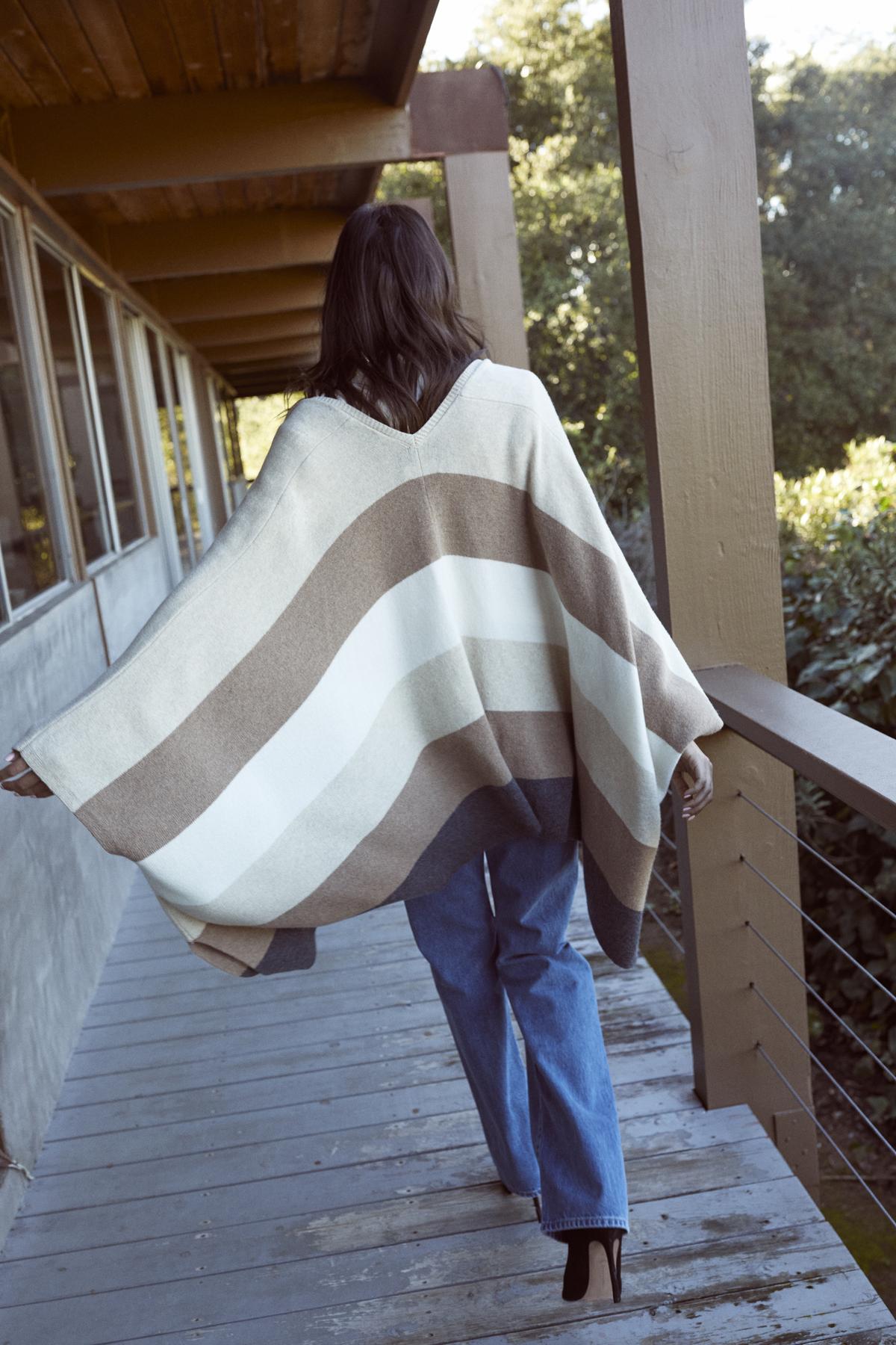   A woman wearing a Velvet by Graham & Spencer JONAS STRIPED OPEN FRONT PONCHO walking on a deck. 