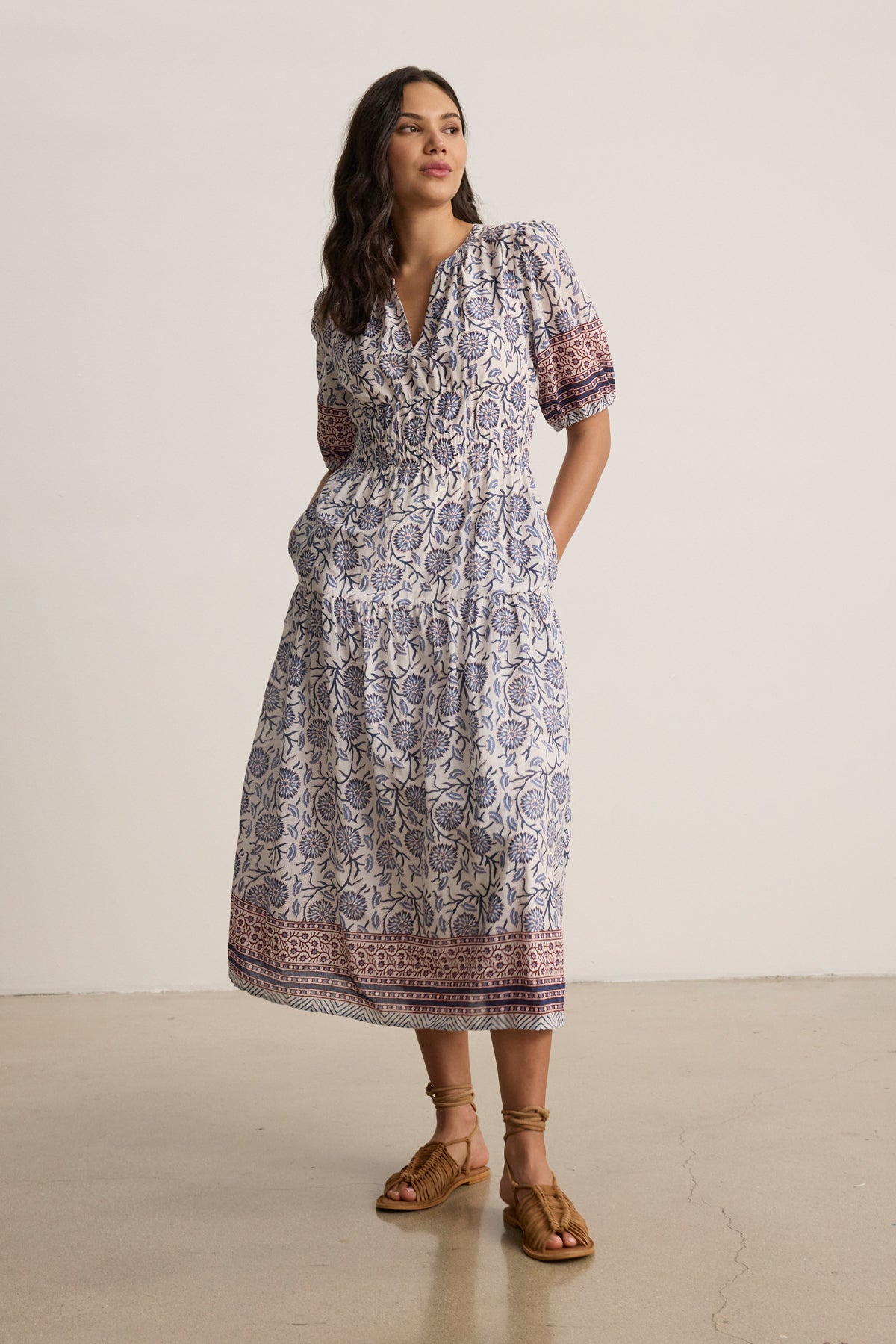 A woman stands indoors wearing the NATALIA DRESS by Velvet by Graham & Spencer, a printed cotton A-line with short sleeves and a v-neckline, styled with brown lace-up sandals.-39488817135809