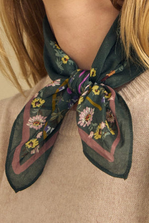A person wearing the MARIANNA SCARF by Velvet by Graham & Spencer, a green floral printed scarf tied around their neck over a light beige sweater.