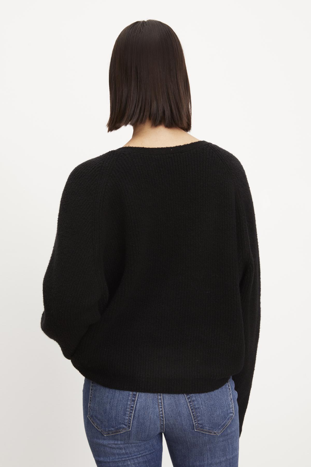 The back view of a woman wearing a Velvet by Graham & Spencer CAITLYN BOUCLE RAGLAN SWEATER with a twist knot detail.-36094304682177