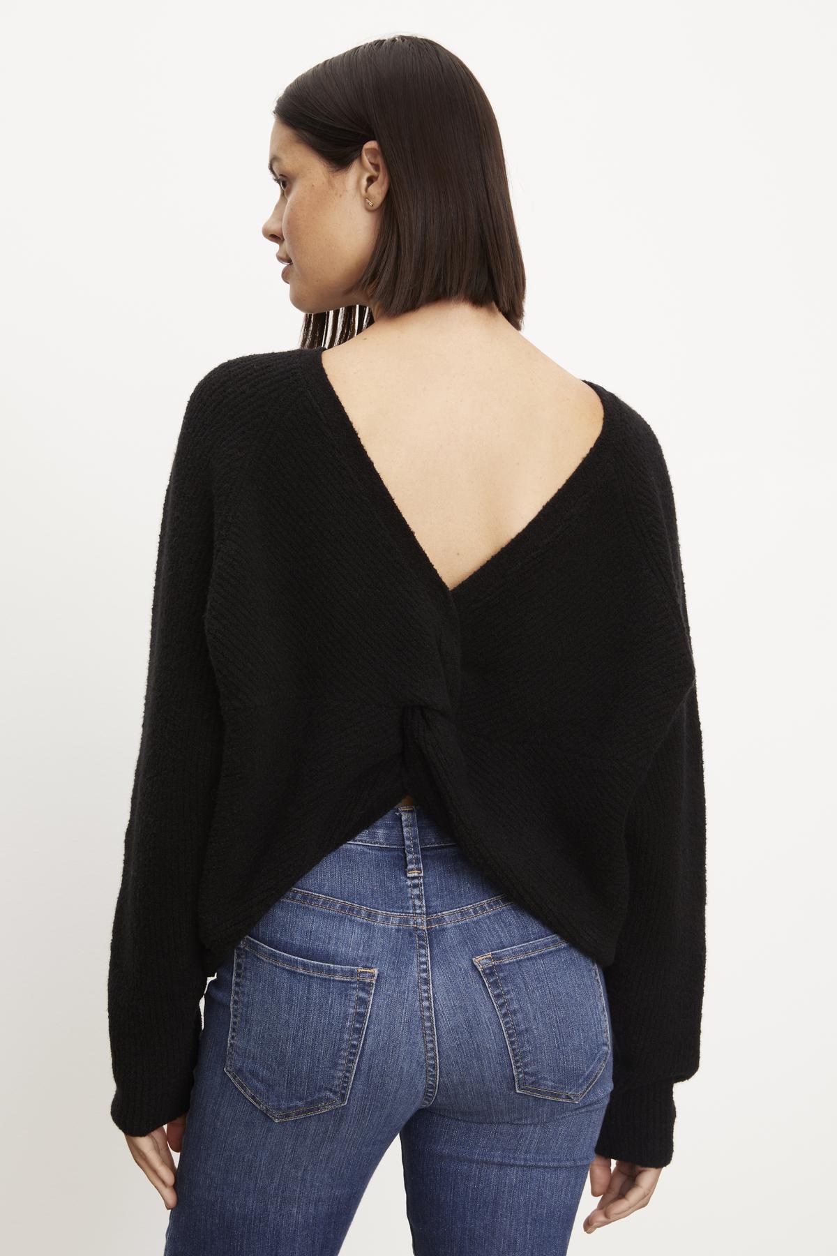 The back view of a woman wearing a black Velvet by Graham & Spencer Caitlyn Boucle Raglan sweater and jeans.-36094304649409