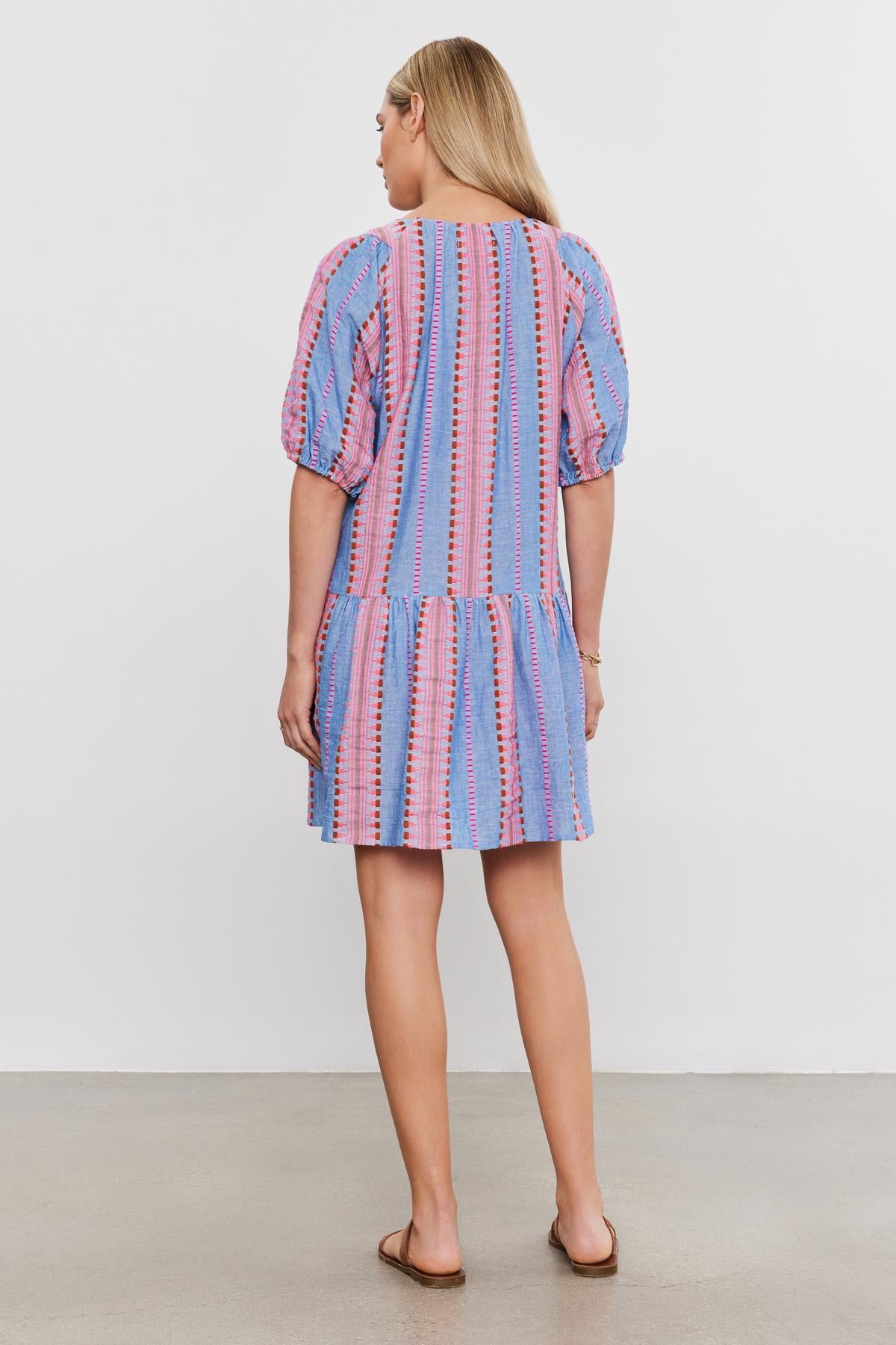 Woman standing with her back to the camera, wearing a short blue and pink striped cotton jacquard ZOELLE DRESS with puff sleeves by Velvet by Graham & Spencer.-36910102347969