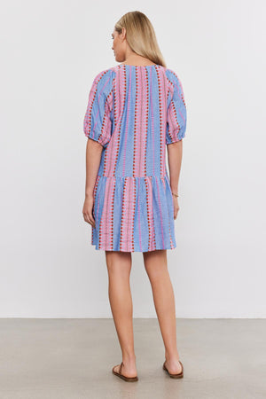 Woman standing with her back to the camera, wearing a short blue and pink striped cotton jacquard ZOELLE DRESS with puff sleeves by Velvet by Graham & Spencer.