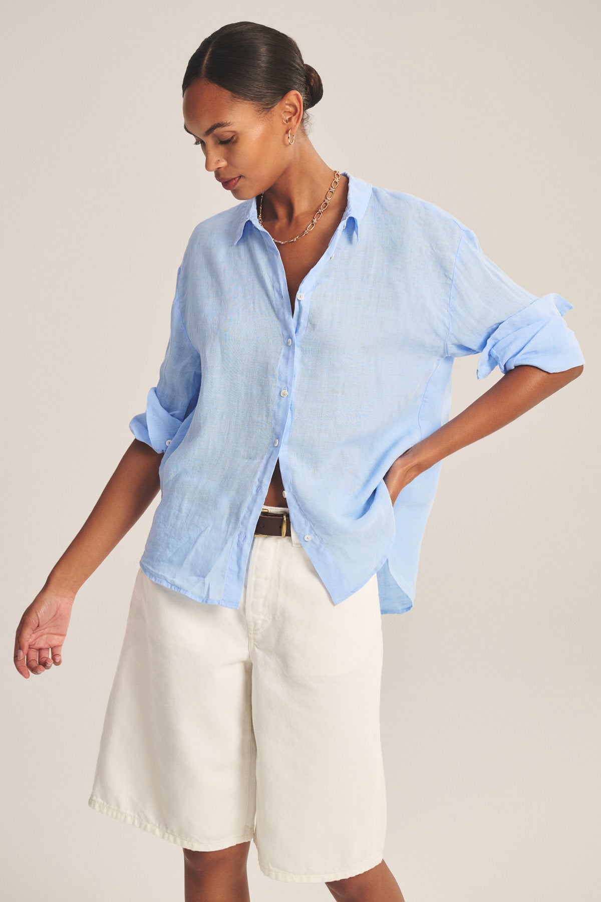 A person wears the BRIGHTON LINEN SHIRT by Velvet by Graham & Spencer, a breathable woven linen button-up with rolled sleeves, paired with relaxed fit white knee-length shorts, standing against a neutral background.