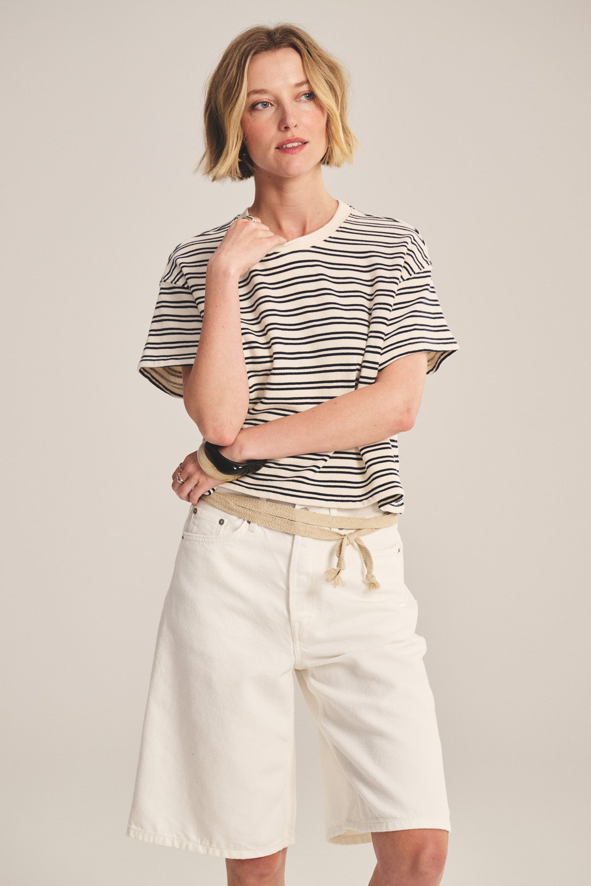 A woman stands against a plain background wearing the BRISSA TOP by Velvet by Graham & Spencer, a vintage stripe cotton t-shirt, paired with loose white knee-length shorts.