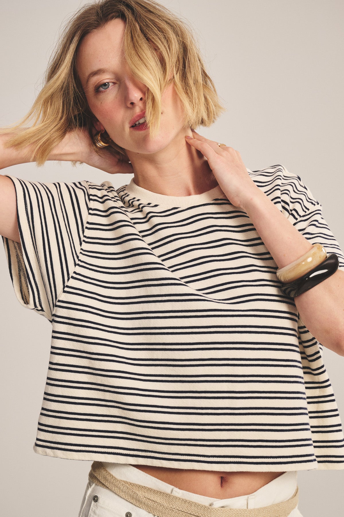 Wearing the BRISSA TOP by Velvet by Graham & Spencer—a relaxed fit, black and white vintage stripe cotton crop top—a person in light pants poses with one hand on their neck and the other behind their head.-40909700825281