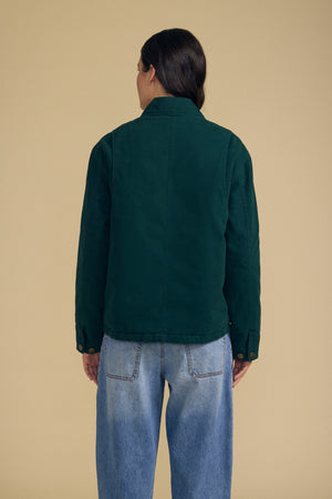 A person stands with their back to the camera, wearing the Velvet by Graham & Spencer DYLAN BARN JACKET in dark green and light blue jeans, set against a plain beige background.
