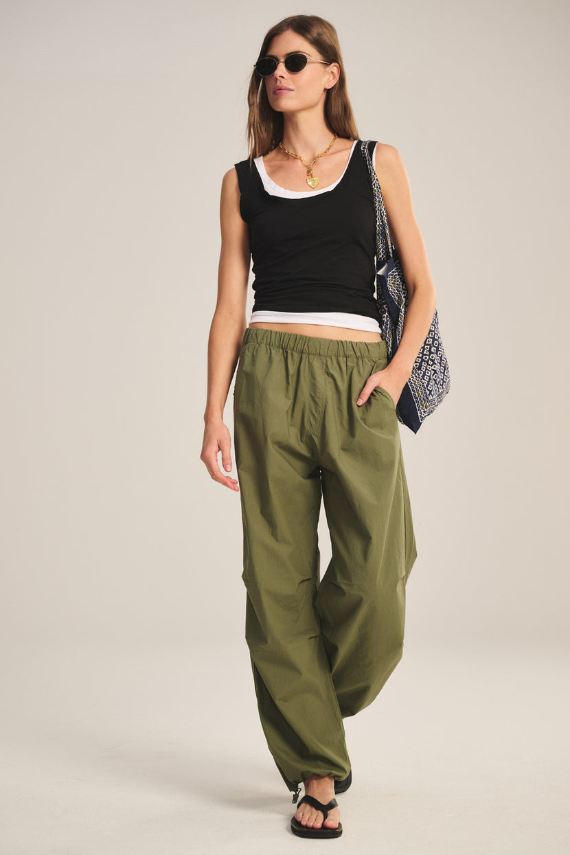 Woman wearing sunglasses, a black tank top over a white undershirt, Velvet by Graham & Spencer BROOKS PANT in olive green poplin with a billowy fit, black sandals, and carrying a patterned tote bag.