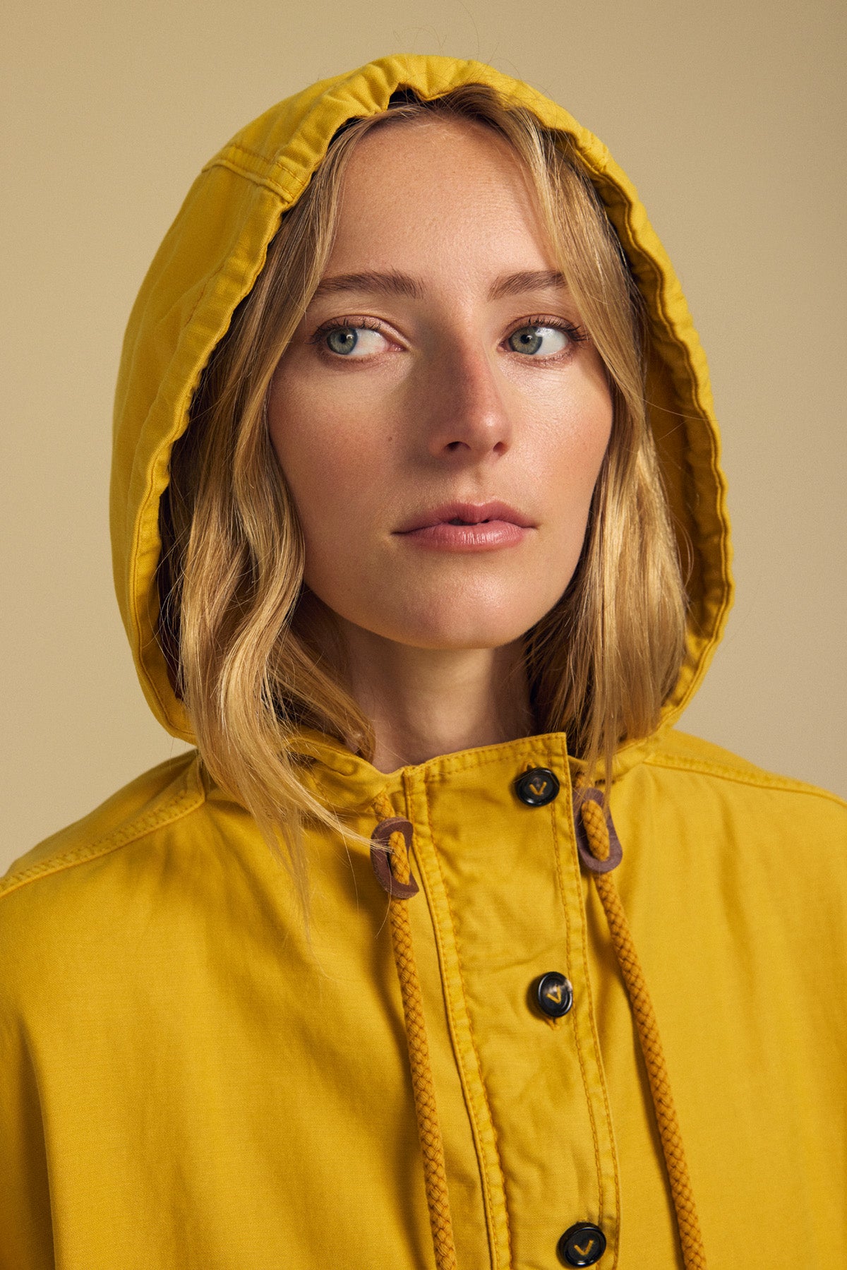 A woman models the BOBBIE HOODIE by Velvet by Graham & Spencer, featuring an oversized yellow silhouette, as she gazes slightly to the side against a plain beige background.
