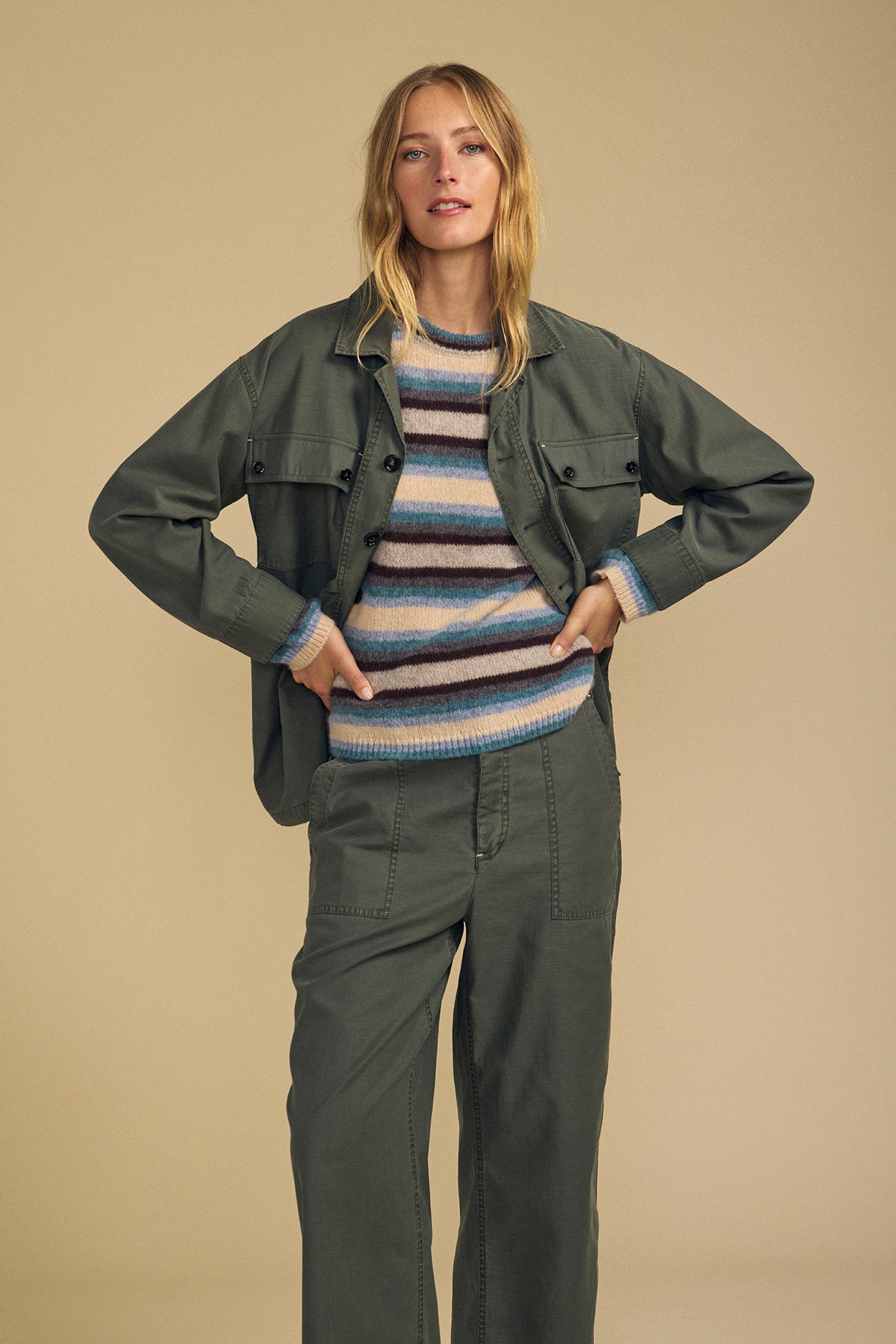 Woman stands facing forward in the KAY SHIRT JACKET by Velvet by Graham & Spencer over a striped sweater and pants, against a plain beige background.