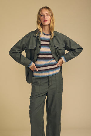 Woman stands facing forward in the KAY SHIRT JACKET by Velvet by Graham & Spencer over a striped sweater and pants, against a plain beige background.
