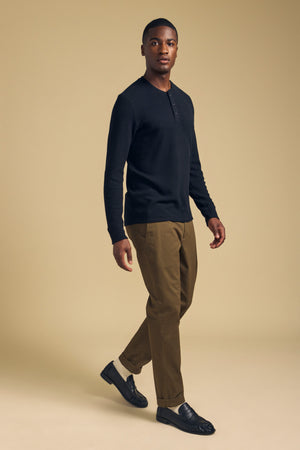 A man wearing a black ROEN THERMAL HENLEY, olive trousers, and black loafers.