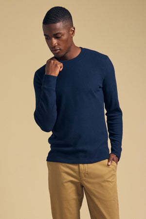 A man wearing a navy blue Velvet by Graham & Spencer TOLLIVER THERMAL CREW PULLOVER and tan trousers.