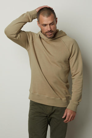 A man wearing a HOPKIN PULLOVER HOODIE by Velvet by Graham & Spencer and green pants crafted for comfort.