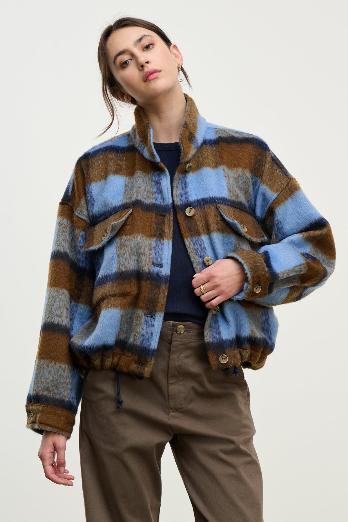A person wears the AUBREY JACKET by Velvet by Graham & Spencer—featuring a blue, brown, and gray plaid pattern, flap pockets, and a stand-up collar—with khaki pants against a plain light background.-39814813647041
