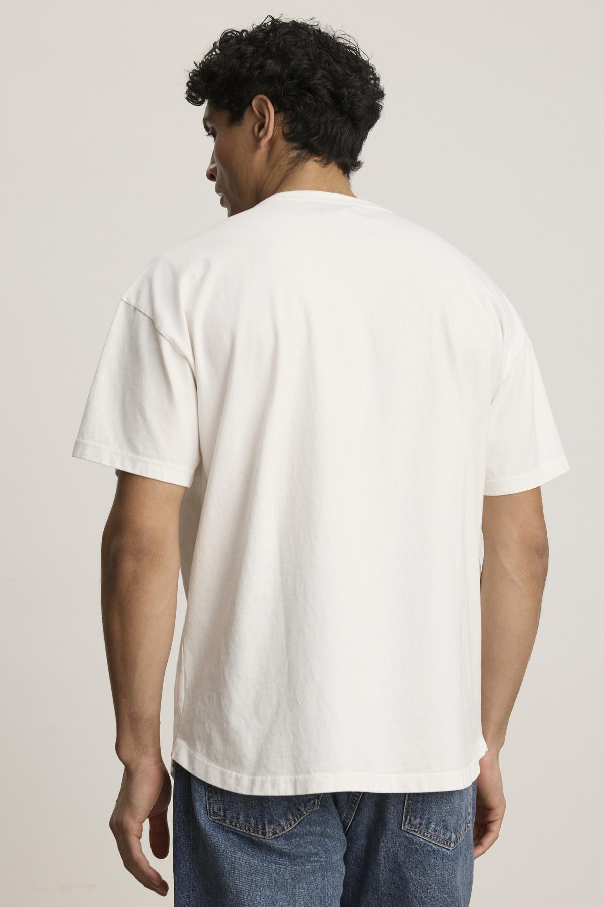   A person in the Velvet by Graham & Spencer BRYAN TEE, made of soft pima cotton jersey, and blue jeans is facing away against a neutral background, highlighting everyday versatility. 