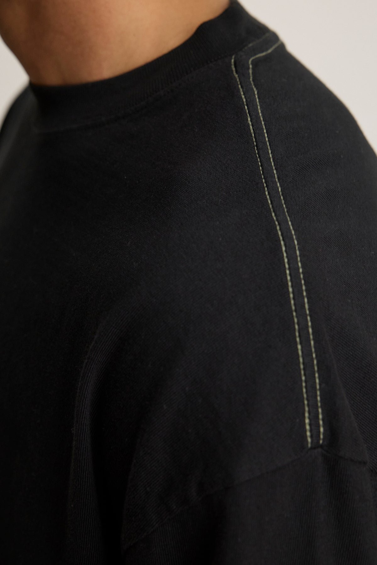   Close-up of someone in the SLATER TEE by Velvet by Graham & Spencer, a black pima cotton jersey shirt with visible white stitching on the shoulder seam. This relaxed fit piece adds versatility to any wardrobe. 